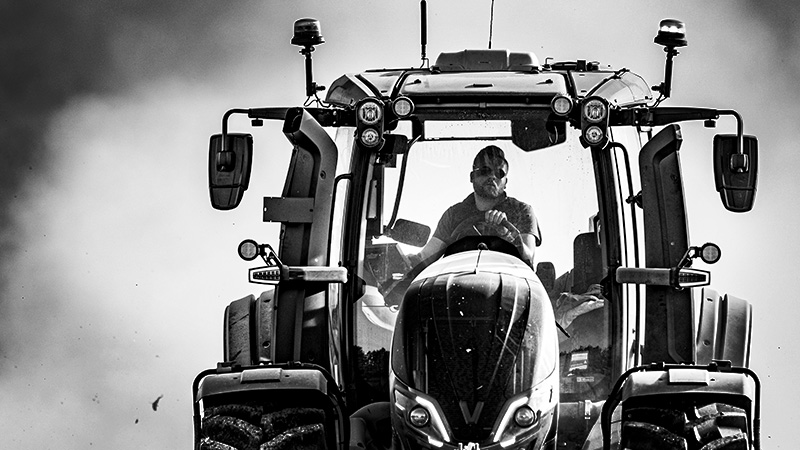 Czarno-białe zdjęcie traktora Valtra serii Q z kierowcą w kabinie podczas prac rolnych