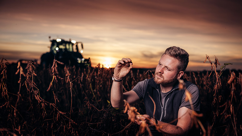 Rolnik sprawdzający plony w polu z traktorem Valtra i zachodzącym słońcem w tle