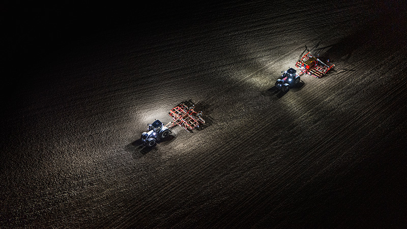 Dwa traktory Valtra pracujące na polu w nocy przy własnym oświetleniu